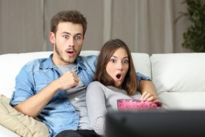 Amazed couple watching tv sitting on a couch at home