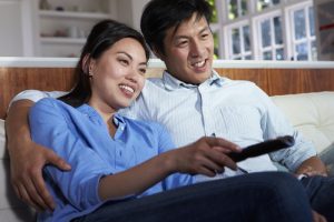 Asian Couple Sitting On Sofa Watching TV Together